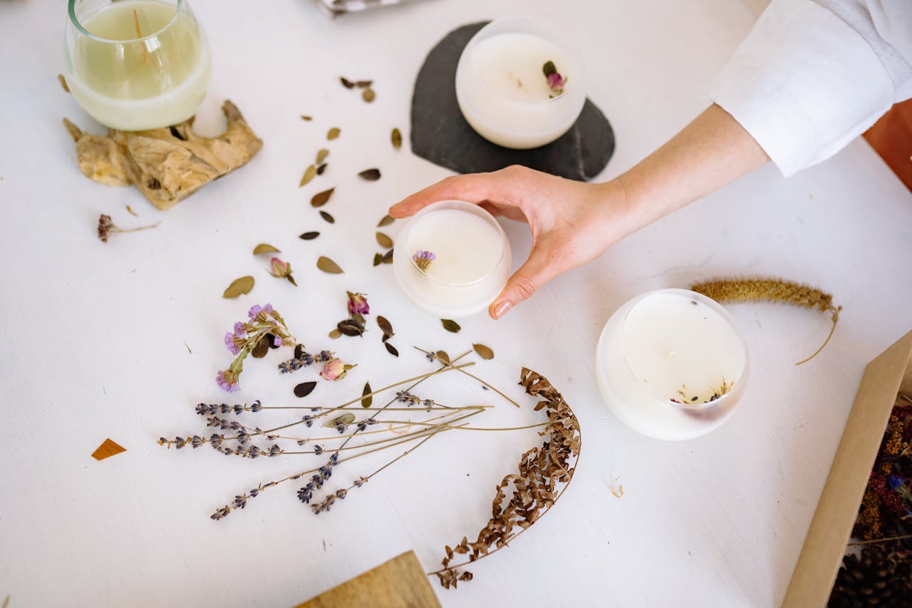 Overhead view of candle making with dried flowers and hands in a workshop.